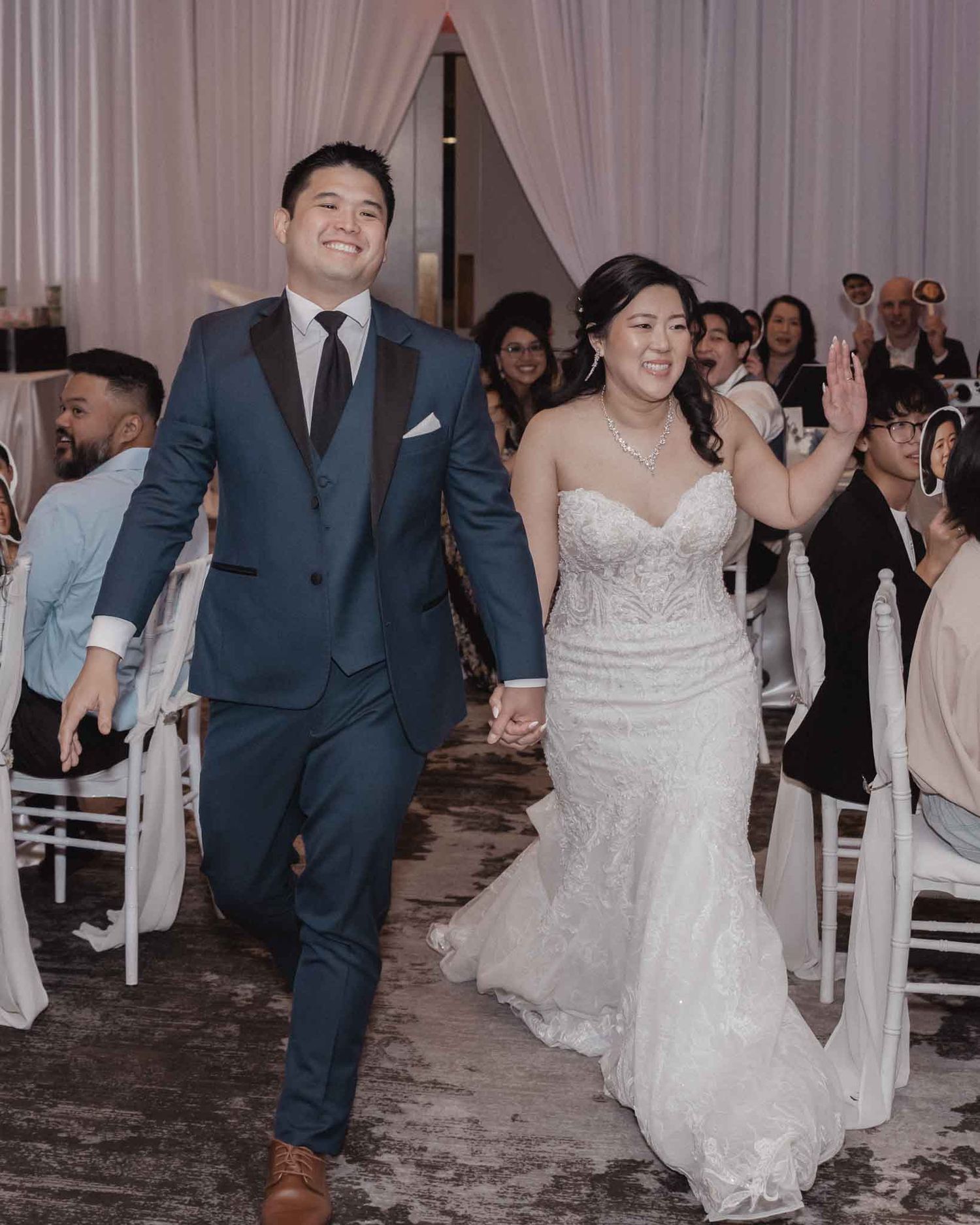 Couple celebrating with guests during their wedding reception in an elegant ballroom setting with soft lighting.