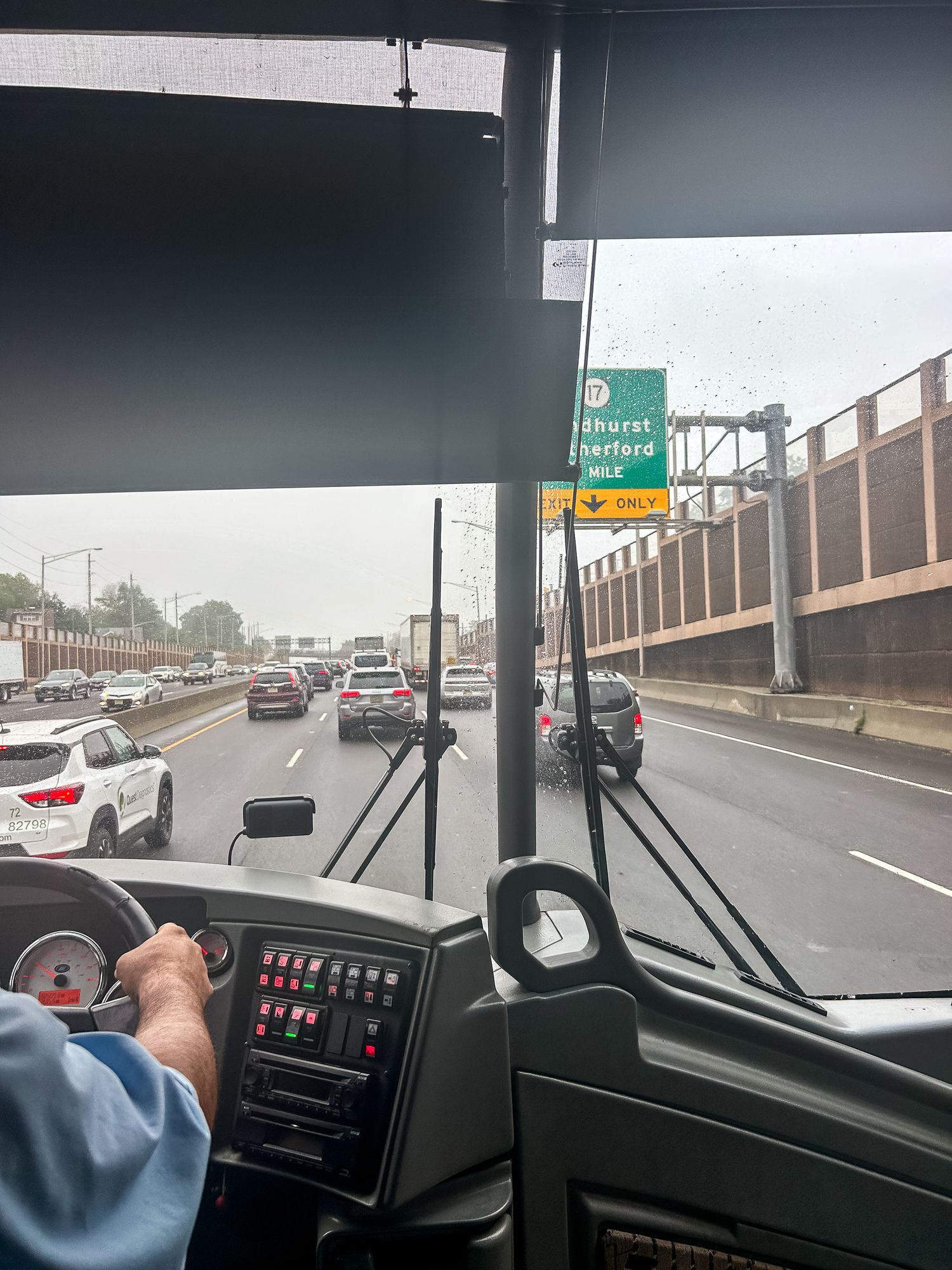 View from driver's seat of vehicle showing highway traffic and overpass signs during overcast conditions.