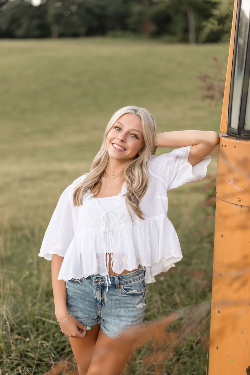 A person in white top and denim shorts poses against an orange rustic door in a grassy outdoor setting.