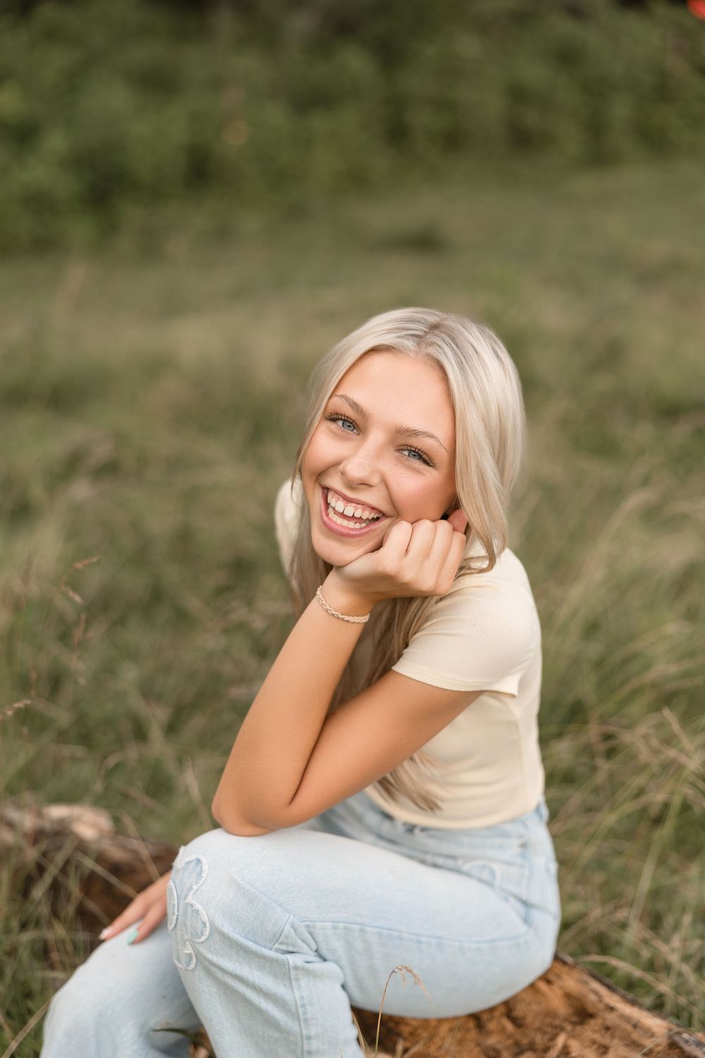 Young woman in casual denim outfit poses outdoors in grassy field with natural lighting and warm expressions.