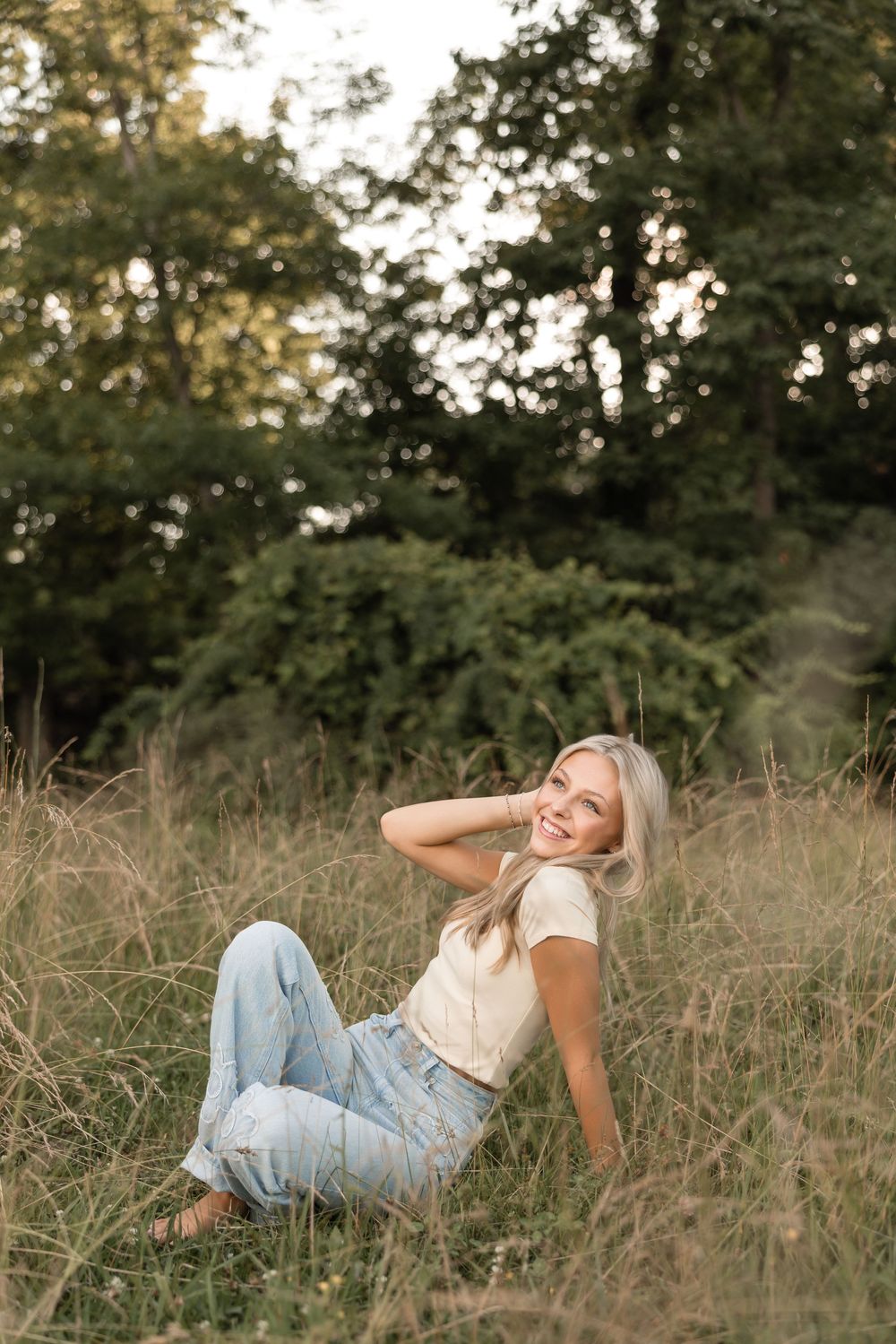 Woman in white t-shirt and distressed jeans lounges in tall grass during golden hour, creating serene outdoor portraits.