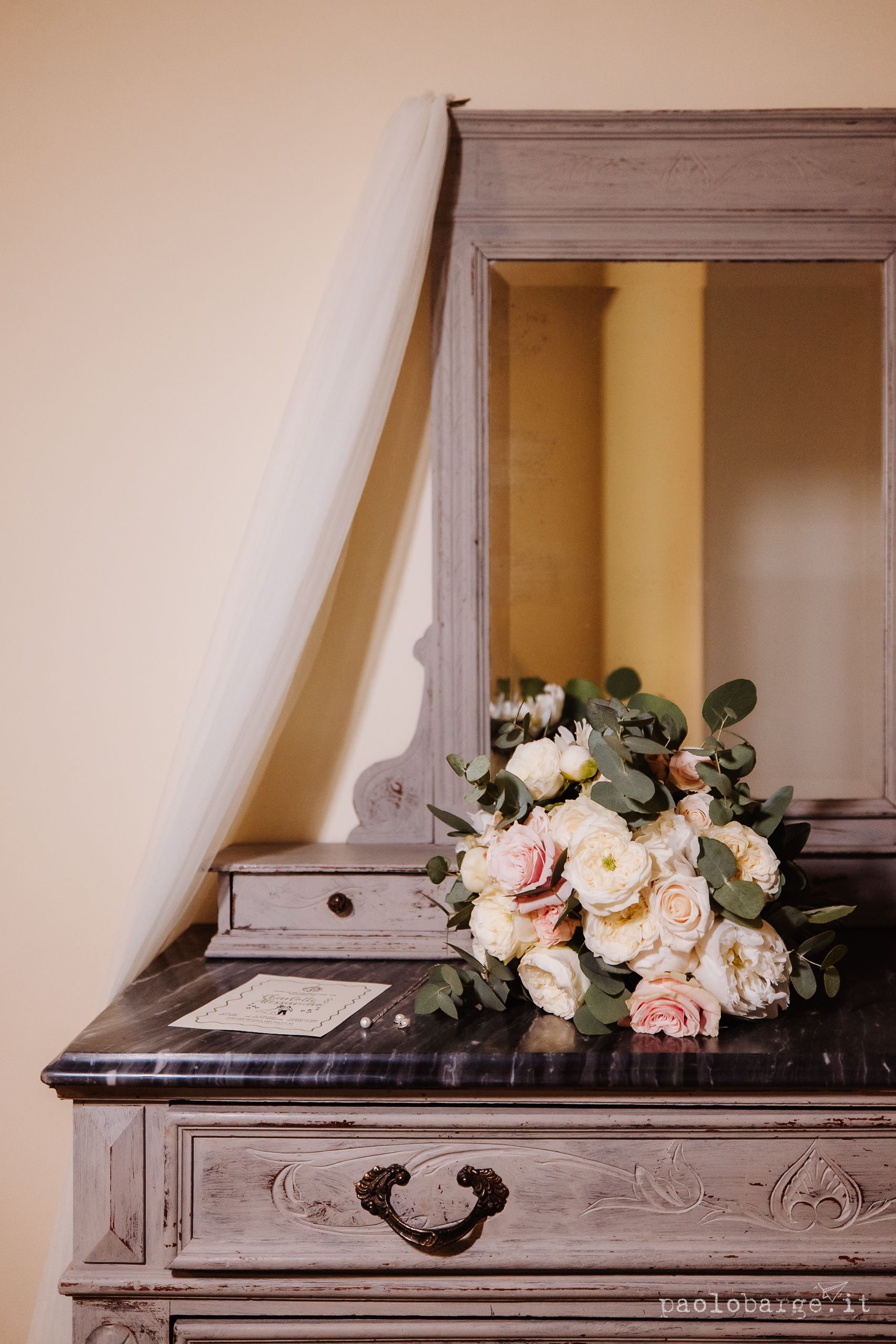 A romantic bouquet of pink and white roses rests on a vintage gray dresser with ornate details and drawer pulls.