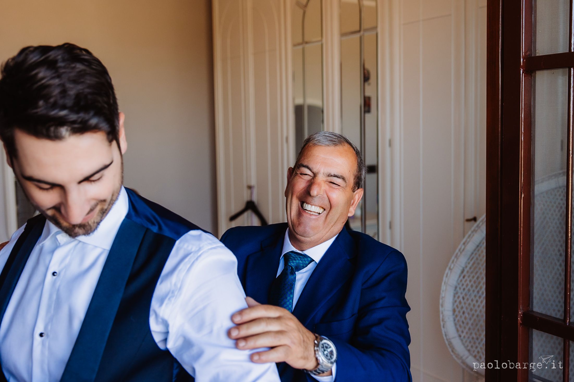 Groomsmen in navy blue suits help each other prepare and adjust their formal attire before a wedding ceremony.