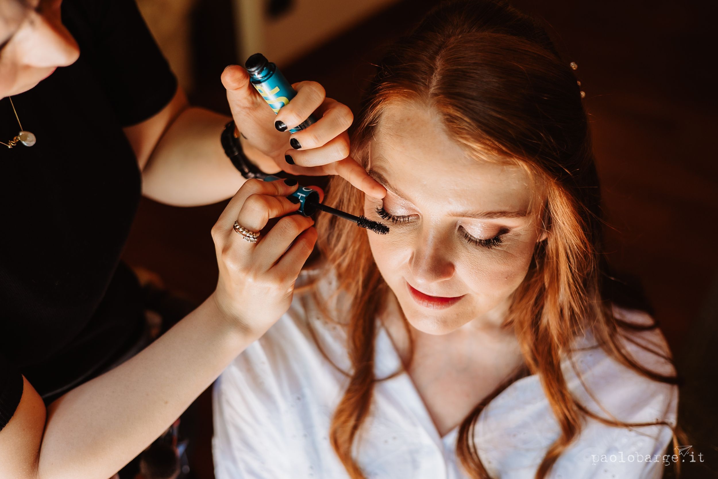 Professional makeup artist applies eye shadow during bridal prep in warm lighting.