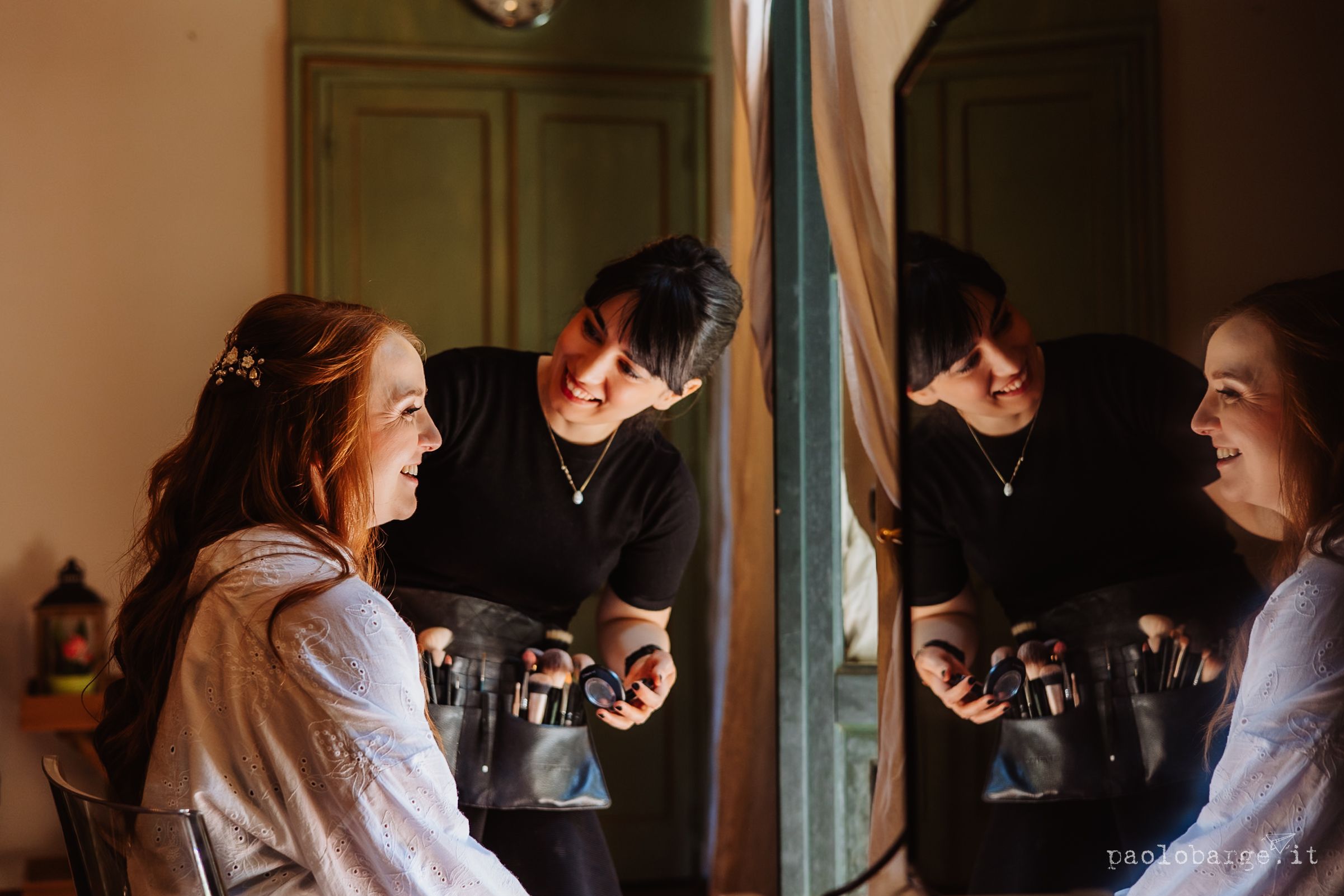 Professional wedding photographer captures candid moments between bride and groom in window light during preparation.