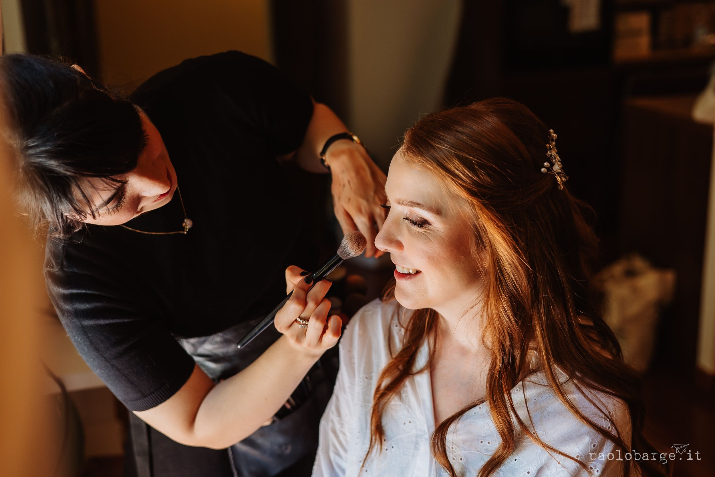 Professional makeup artist applying eyeshadow to client in soft lighting for wedding preparation.
