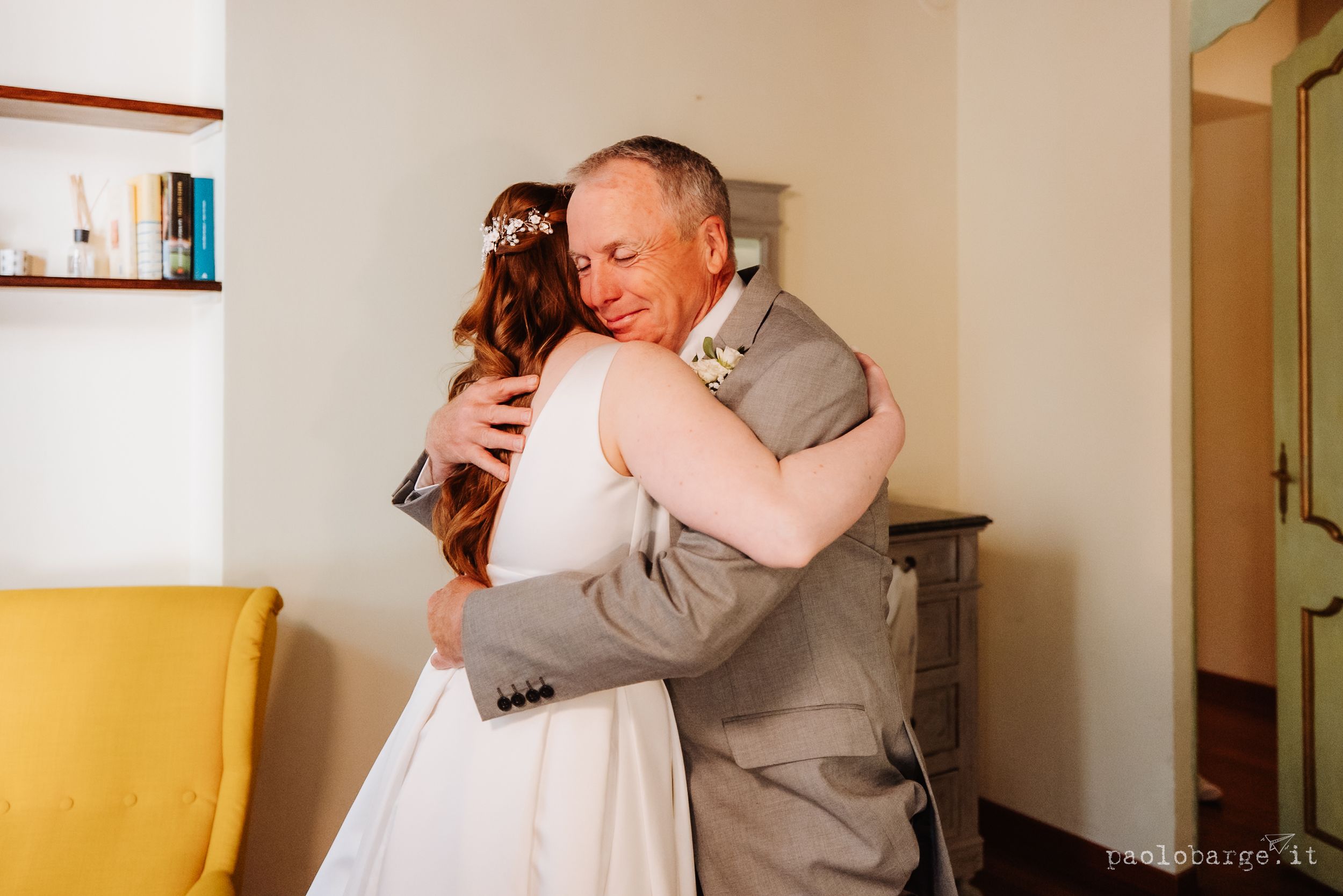 A heartfelt embrace between two people in formal attire, one wearing a white dress and another in a gray suit.