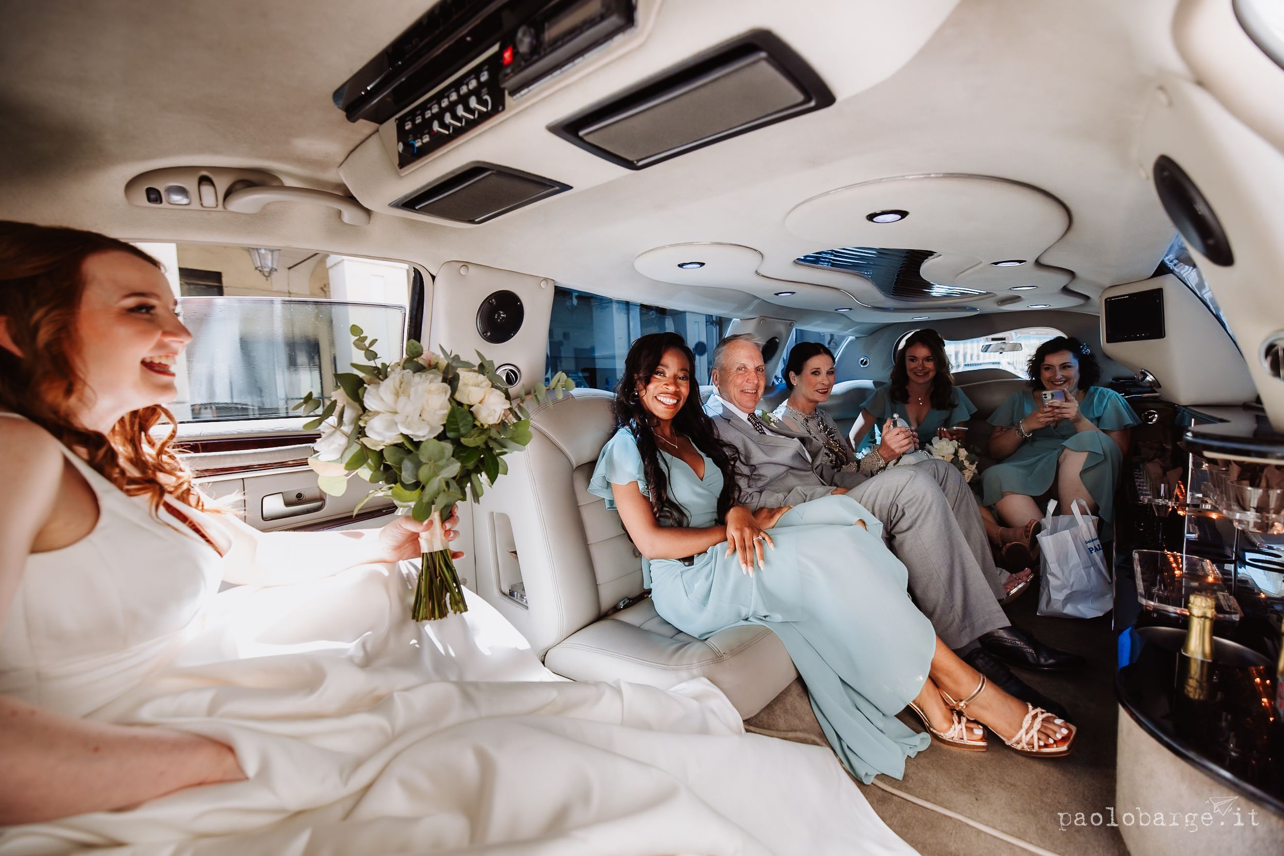Wedding party celebrating inside a luxury limousine with bridesmaids in light blue dresses and flowers.