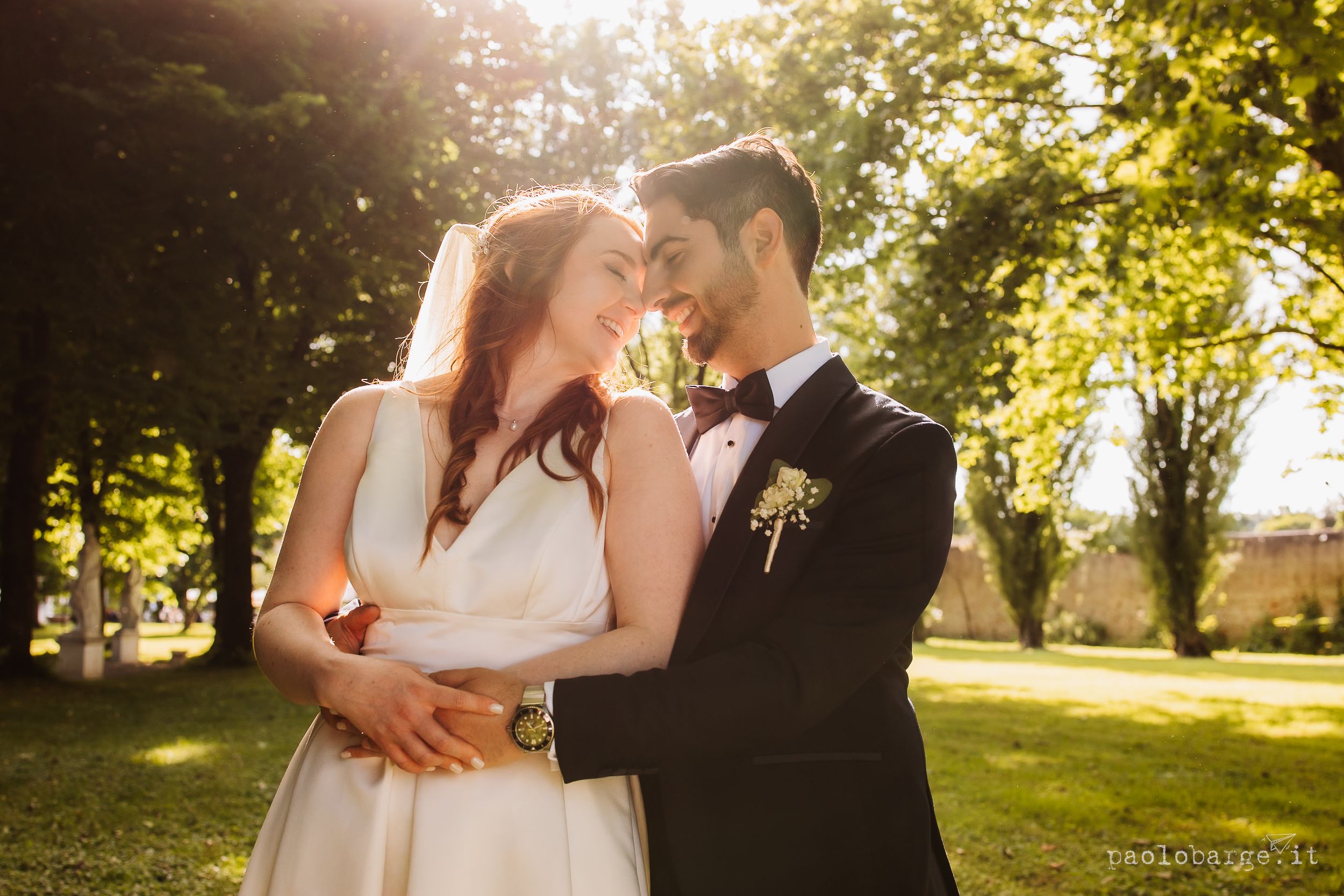 Newlywed couple sharing intimate moments in a sunlit garden setting during golden hour photography session.