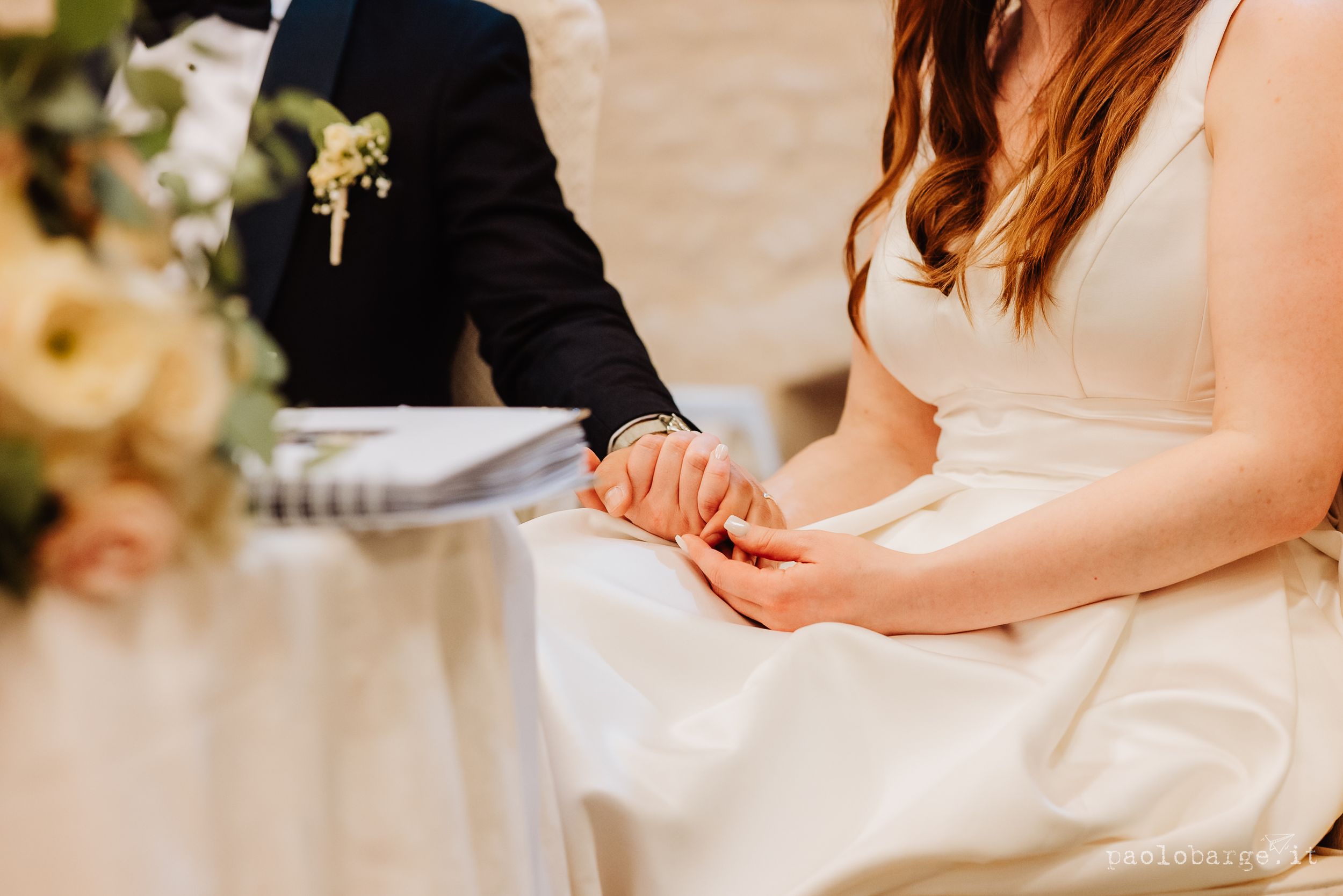Three people in formal attire seated together at an elegant indoor reception table with floral centerpieces.