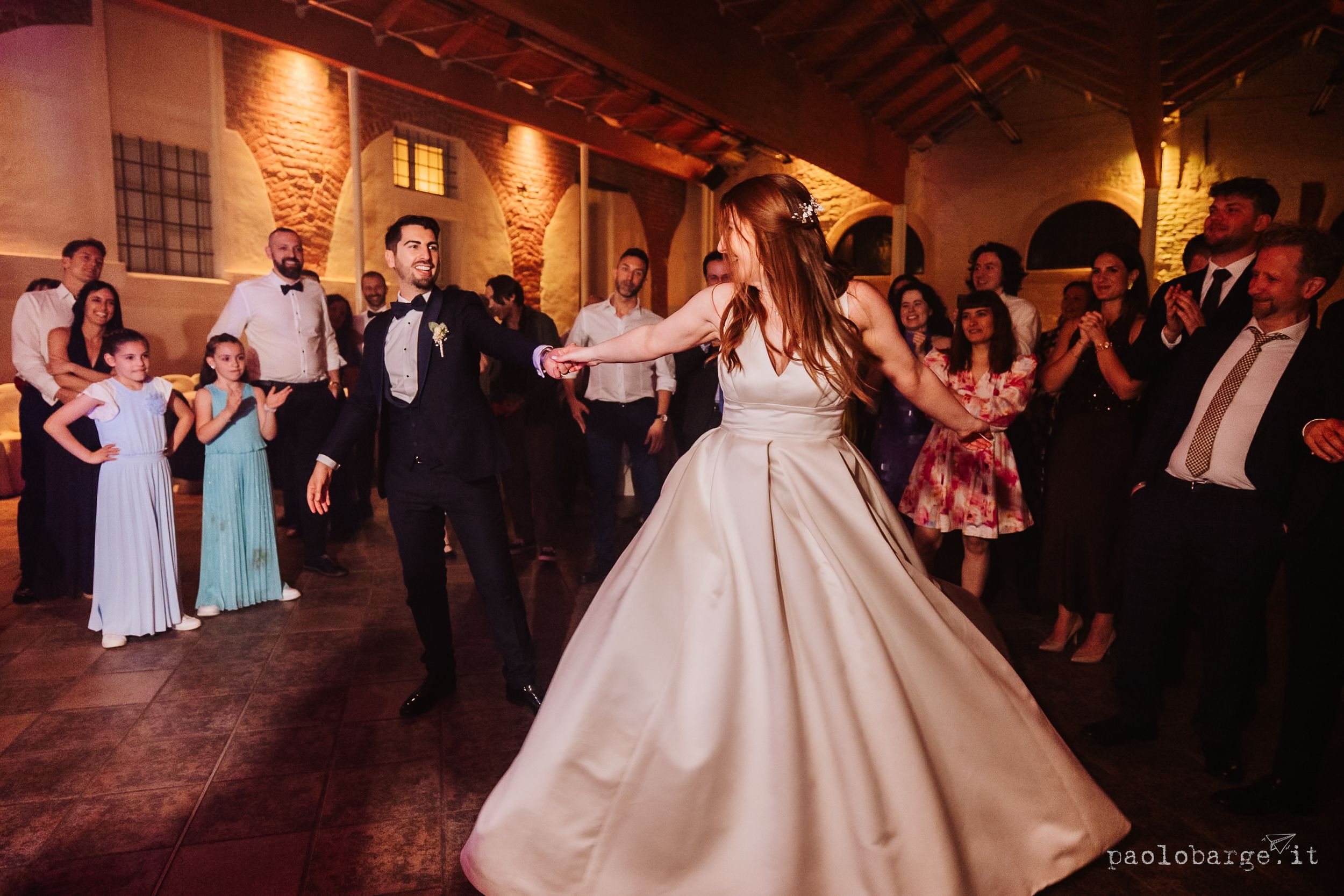 Wedding celebration at a rustic venue with people dancing on a wooden floor beneath warm lighting and exposed beams.