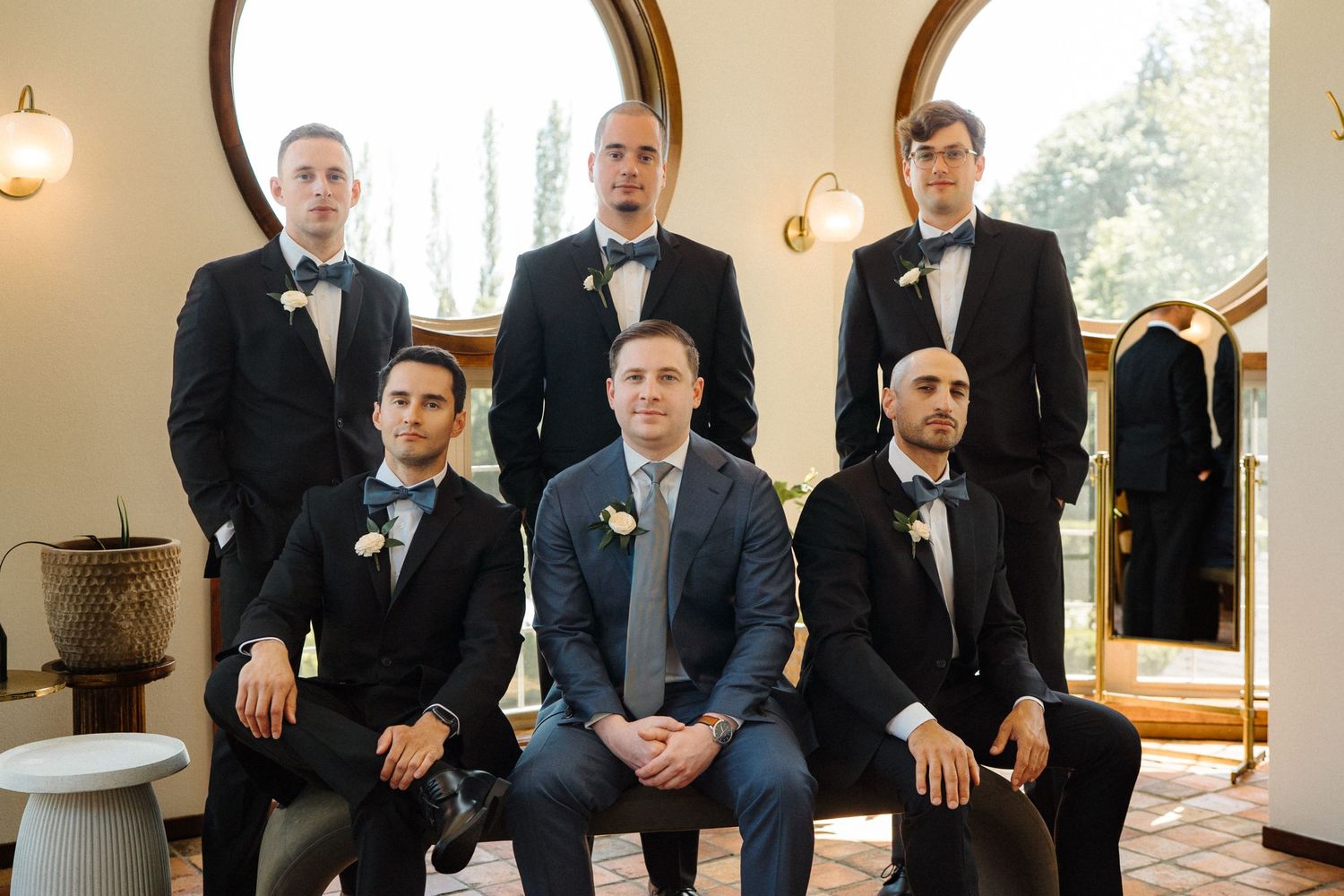 A group in formal black suits and bow ties pose together gracefully on wooden stairs in elegant wedding attire.