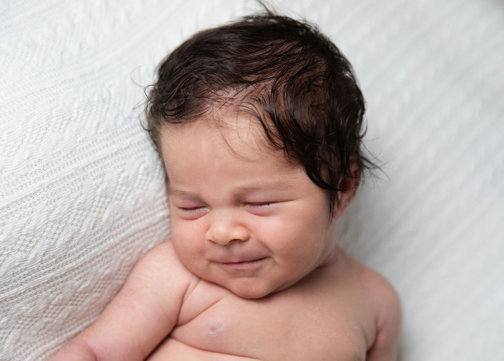 Sweet newborn baby smiles with eyes closed while laying on white textured blanket during a professional newborn family photoshoot in London
