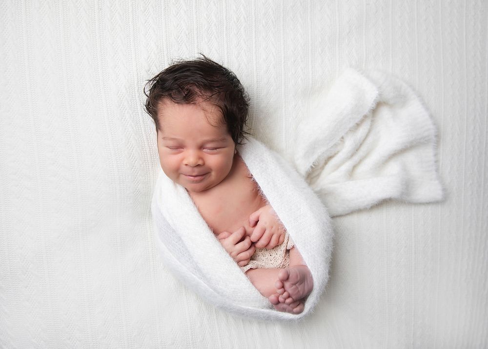 Peaceful newborn baby wrapped in soft white blanket during professional photography session. During a newborn family session in London.