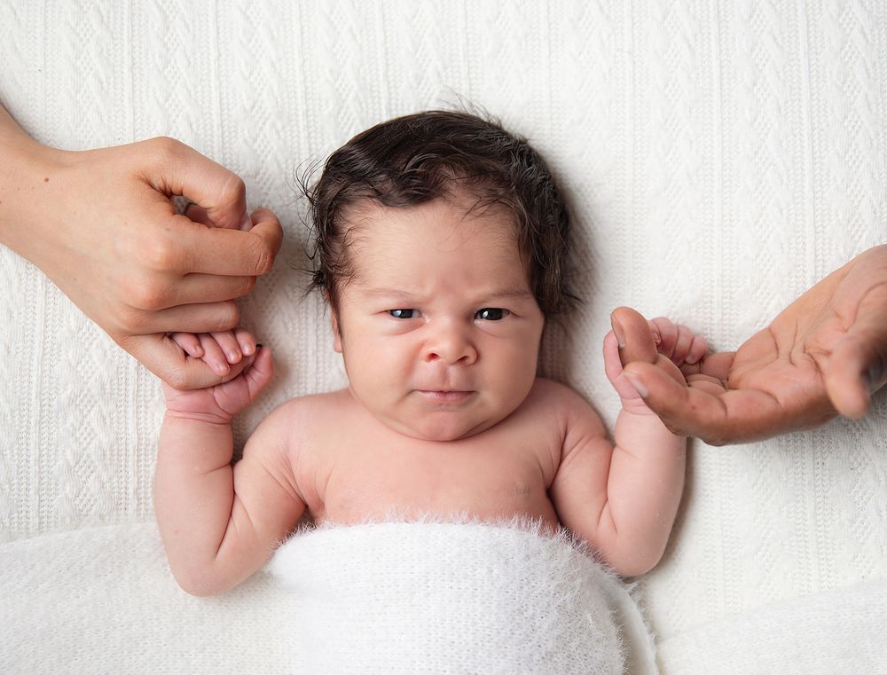 Four connected images show a sleeping newborn baby in white wrappings against a white background. During a newborn family session in London