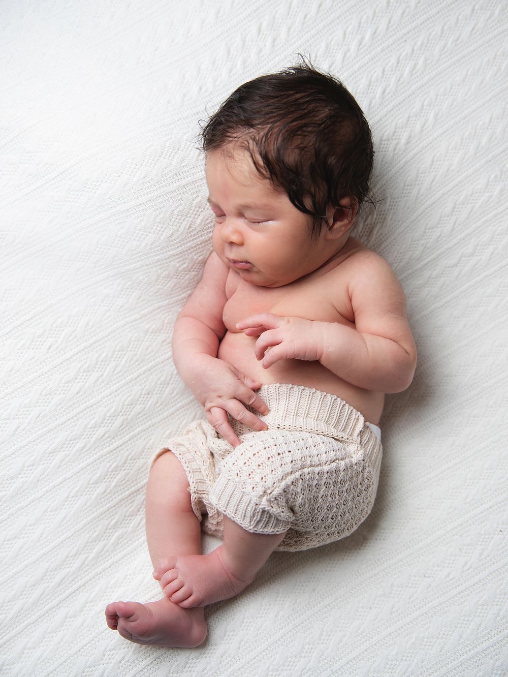 Newborn baby sleeping peacefully on white backdrop wearing knitted wrap in artistic studio portrait composition. During a newborn session
