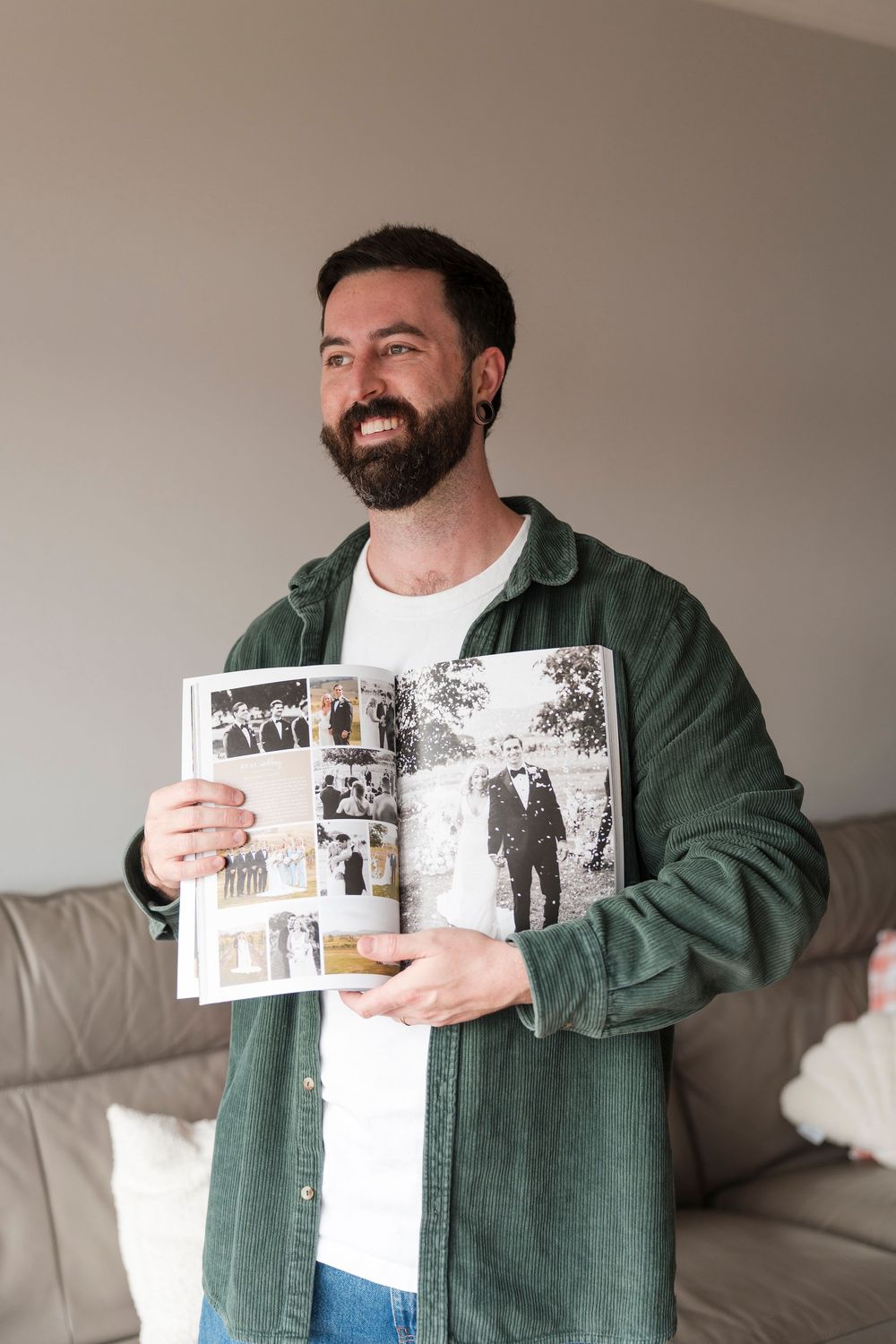 Smiling person wearing a green corduroy shirt holds open a photo album displaying black and white wedding photographs.
