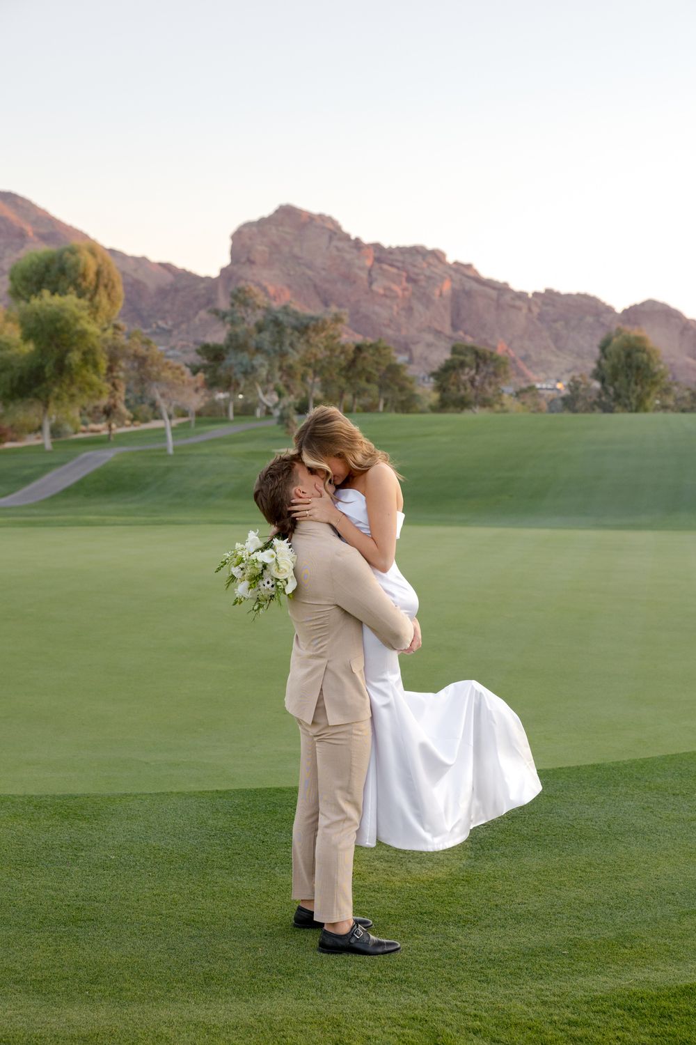 Romantic embrace on golf course green with desert mountains in background during sunset.
