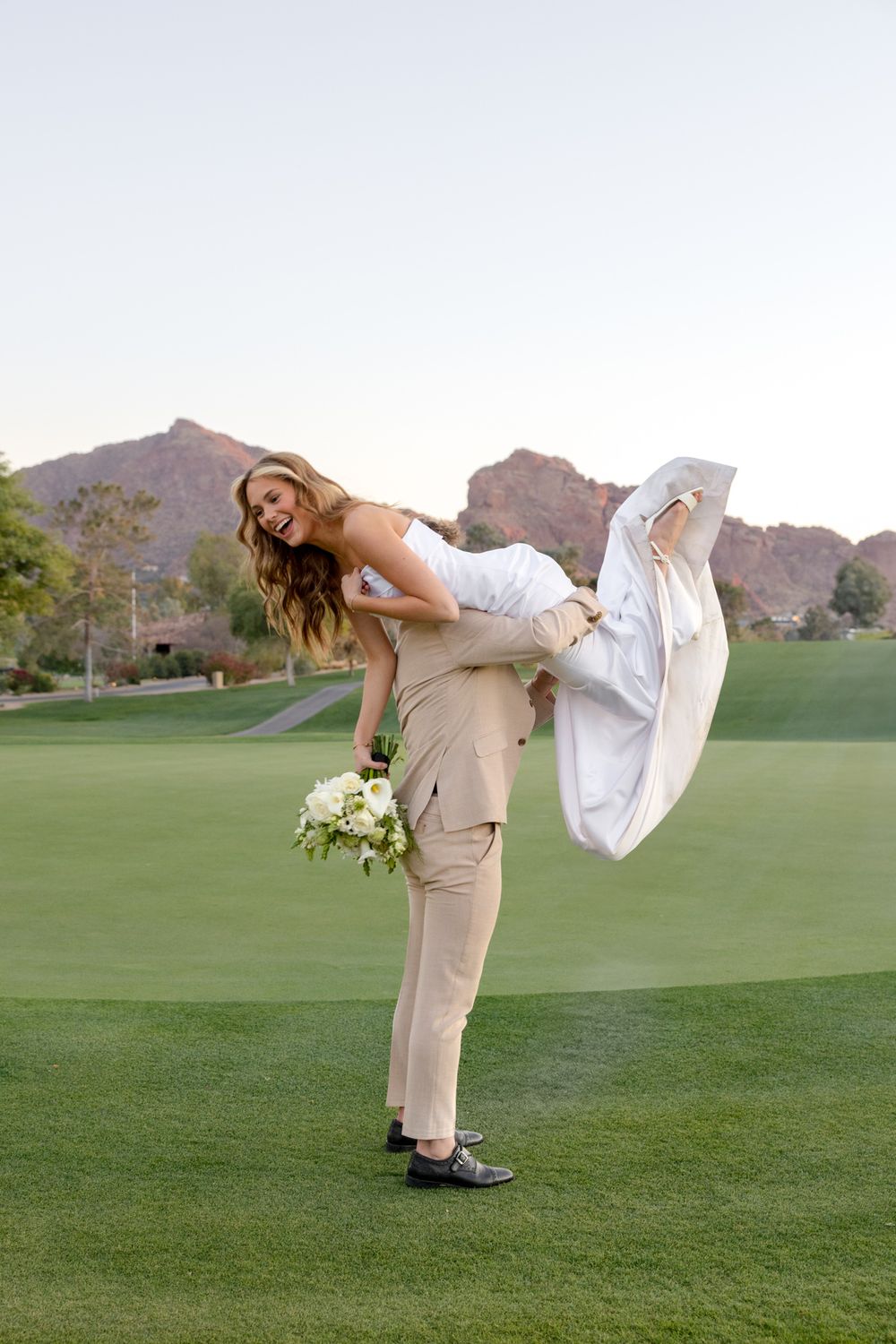 Playful wedding photo on golf course with desert mountains in background.