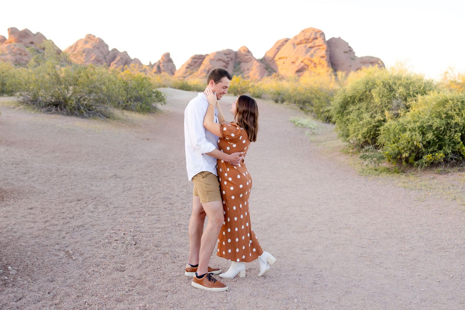 A couple embraces during a desert photo session at Papago Park in Phoenix with red rocks in the background.