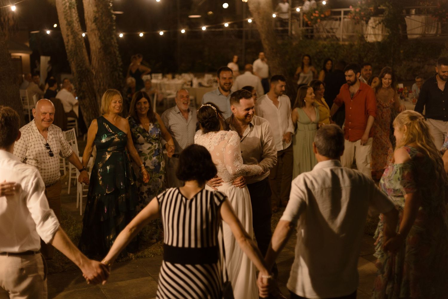 People dancing in a circle at what appears to be a rustic indoor venue with warm lighting and casual atmosphere.