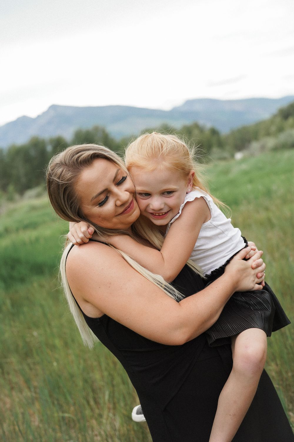 A tender moment shared between two people embracing in a grassy field with mountains in the background.