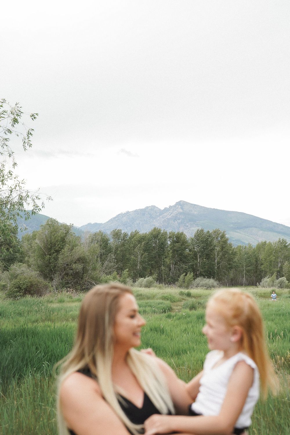 Two people captured in a playful candid moment in a field with mountain views and tall grass.