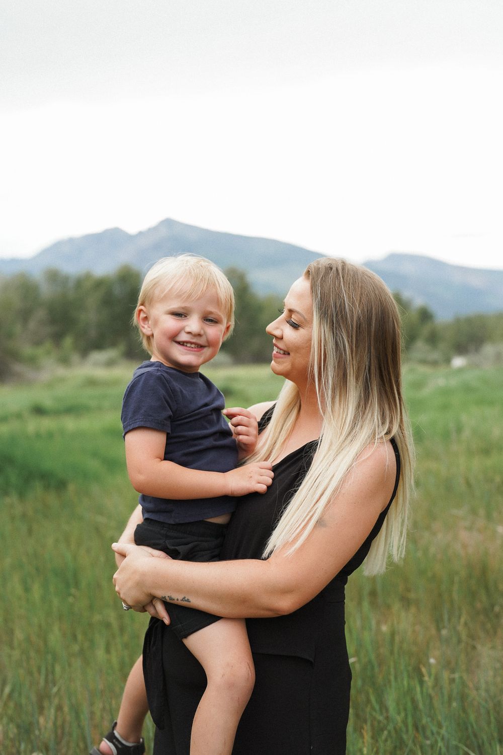 A mother and child sharing joyful moments together in a grassy field with mountains in the background.