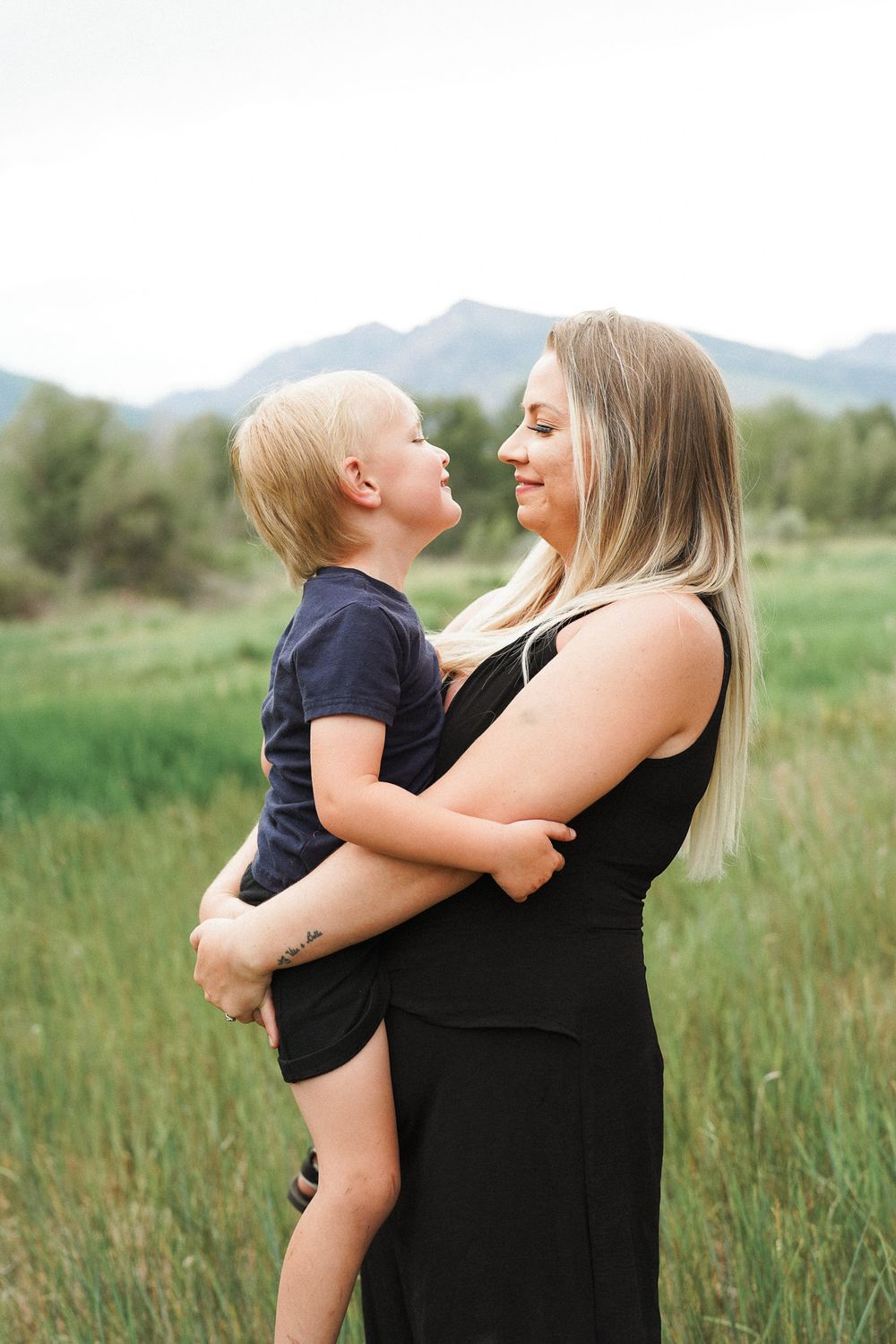 Parent and child share joyful moments together in a grassy field with mountains in the background.