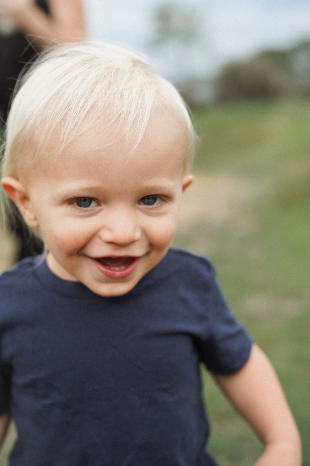 Five sequential images showing a playful toddler in a navy blue shirt expressing joyful emotions against a blurred outdoor background.