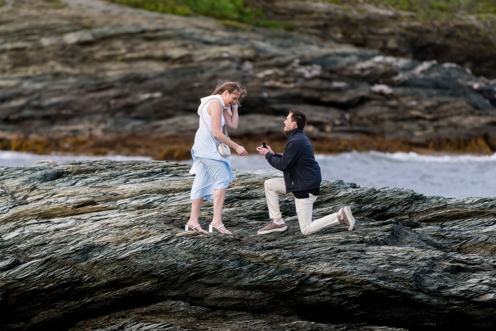 Romantic coastal photo session on rocky cliffs overlooking ocean waves during sunset.
