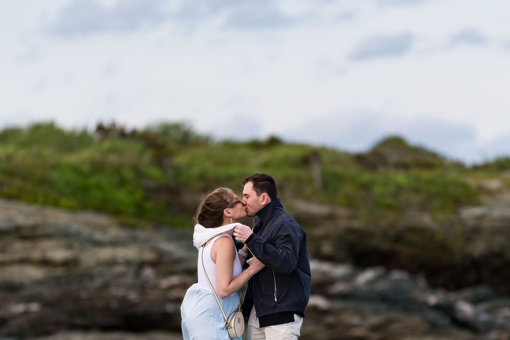 A romantic moment between a couple embracing on rocky coastal cliffs with cloudy skies in the background.