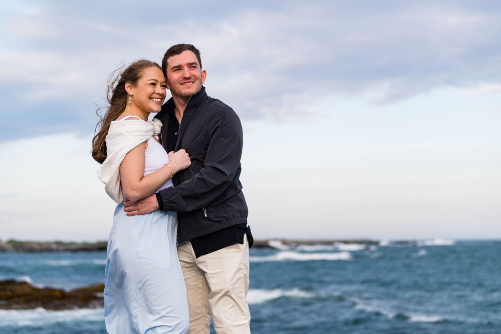 Happy couple sharing intimate moment by the sea with waves and cloudy sky.