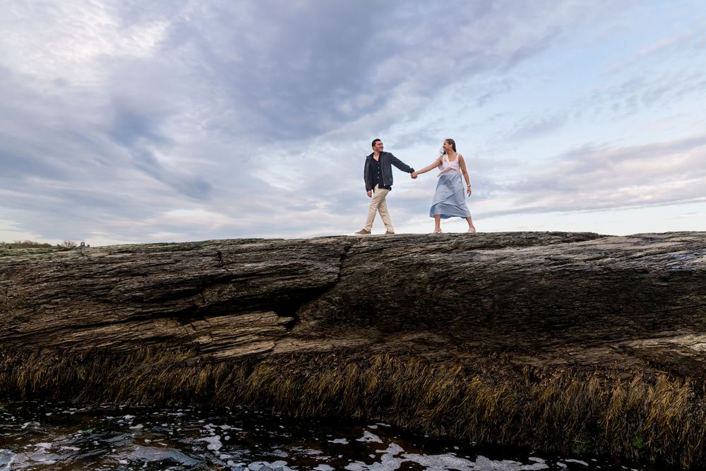 Two people dance together on volcanic rocks by the ocean during a romantic photoshoot.
