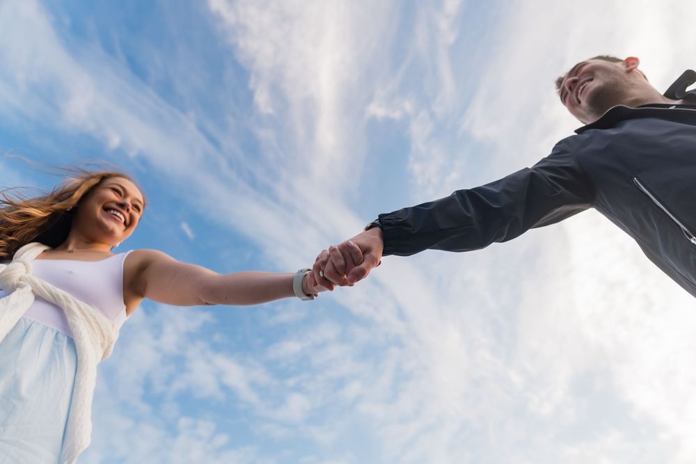 Low angle shot against blue sky showing couple holding hands during coastal photo session.
