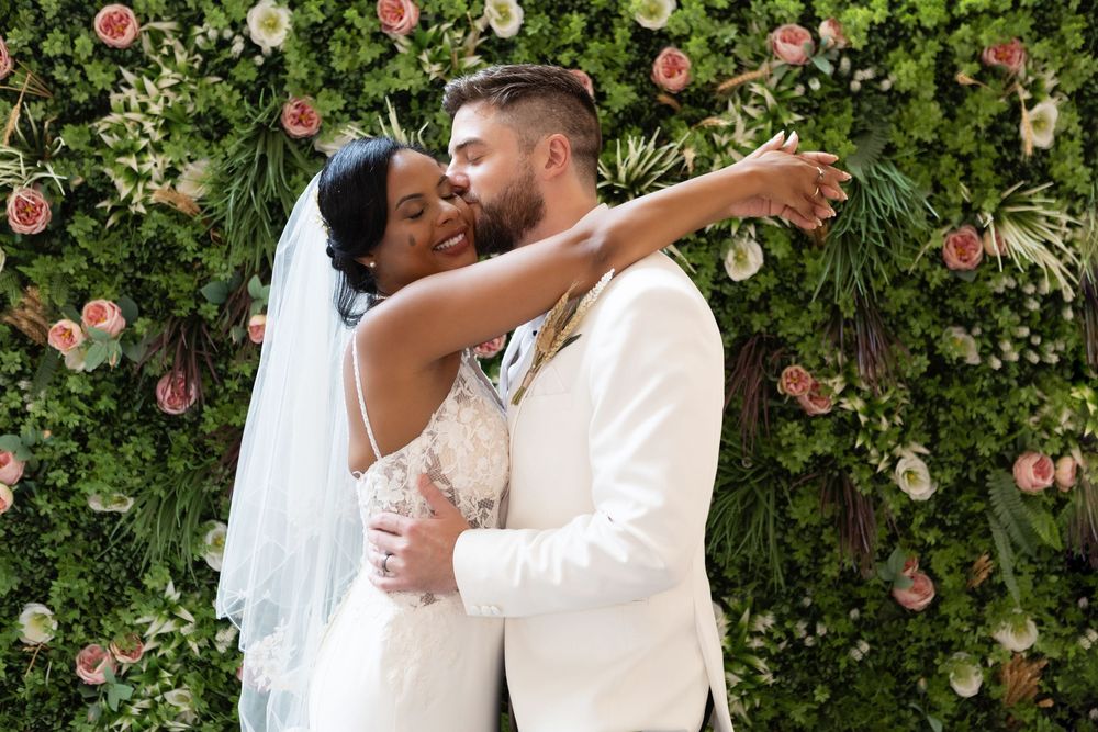 A happy couple shares a romantic dance surrounded by pink roses and green foliage on their wedding day.