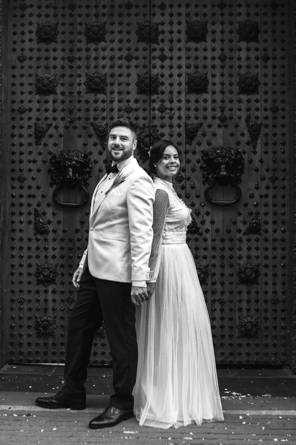 A black and white wedding photo of a couple standing back-to-back against an industrial metal door background.