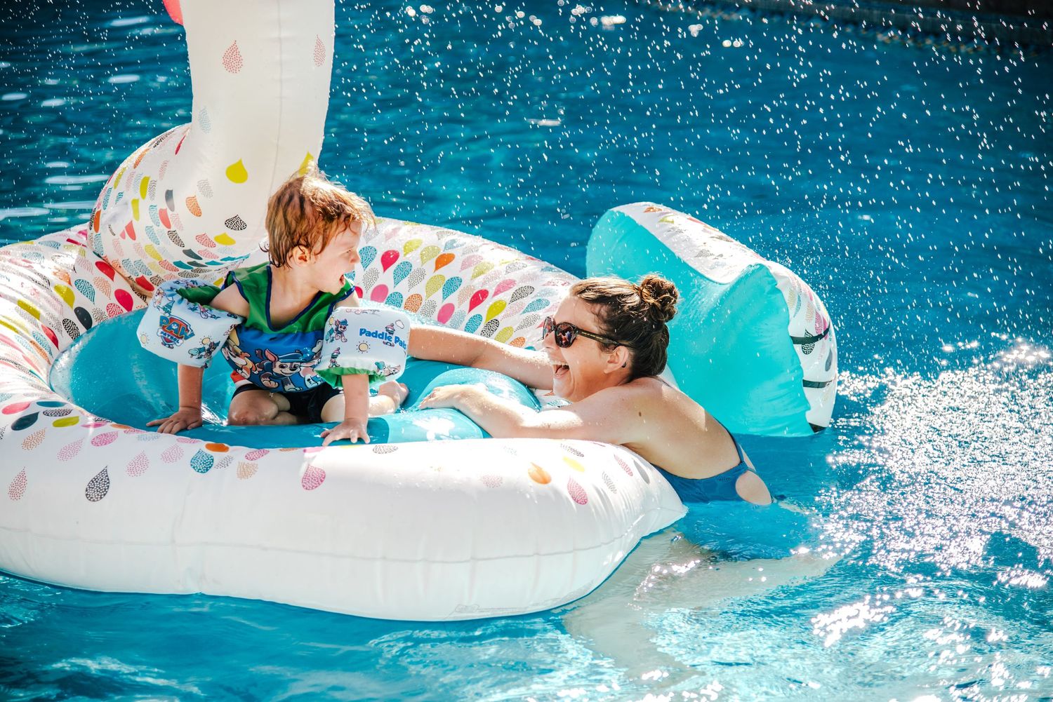 Inflatable pool float with colorful sprinkle pattern splashing in bright blue swimming pool on sunny summer day.