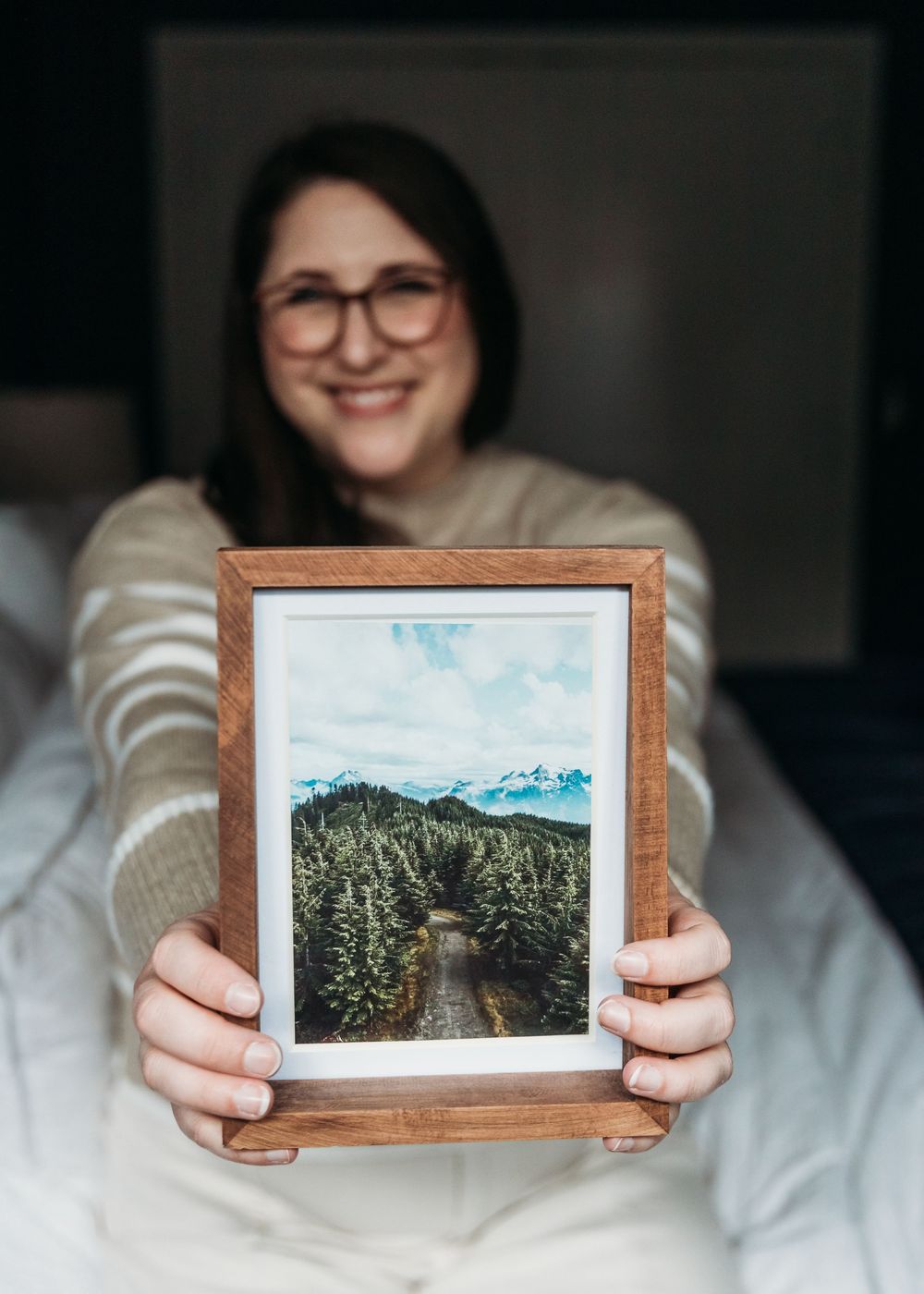 Someone holds a framed photograph showing a scenic mountain road winding through a dense evergreen forest landscape.