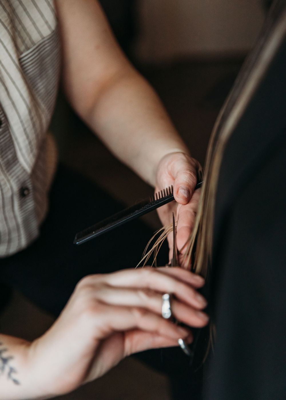 Close-up of hands trimming hair with scissors and comb during a professional haircut session.