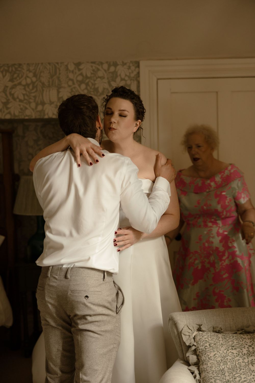 Romantic couple shares an intimate dance moment in a white and grey outfitted wedding scene with floral decor.