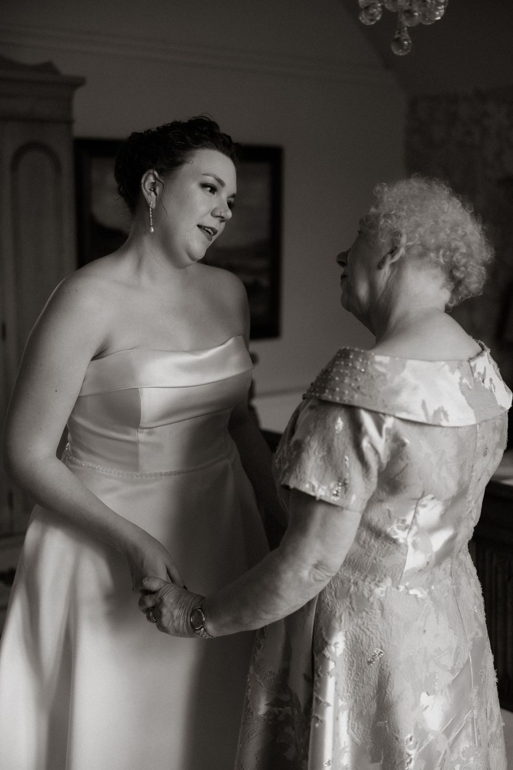 A tender black and white wedding moment shows a person in a strapless gown sharing a special moment with an elderly figure.