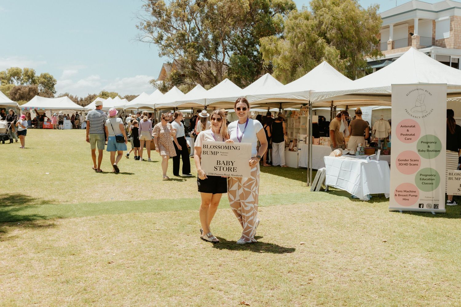 People browsing white vendor tents at an outdoor market fair on a sunny day.