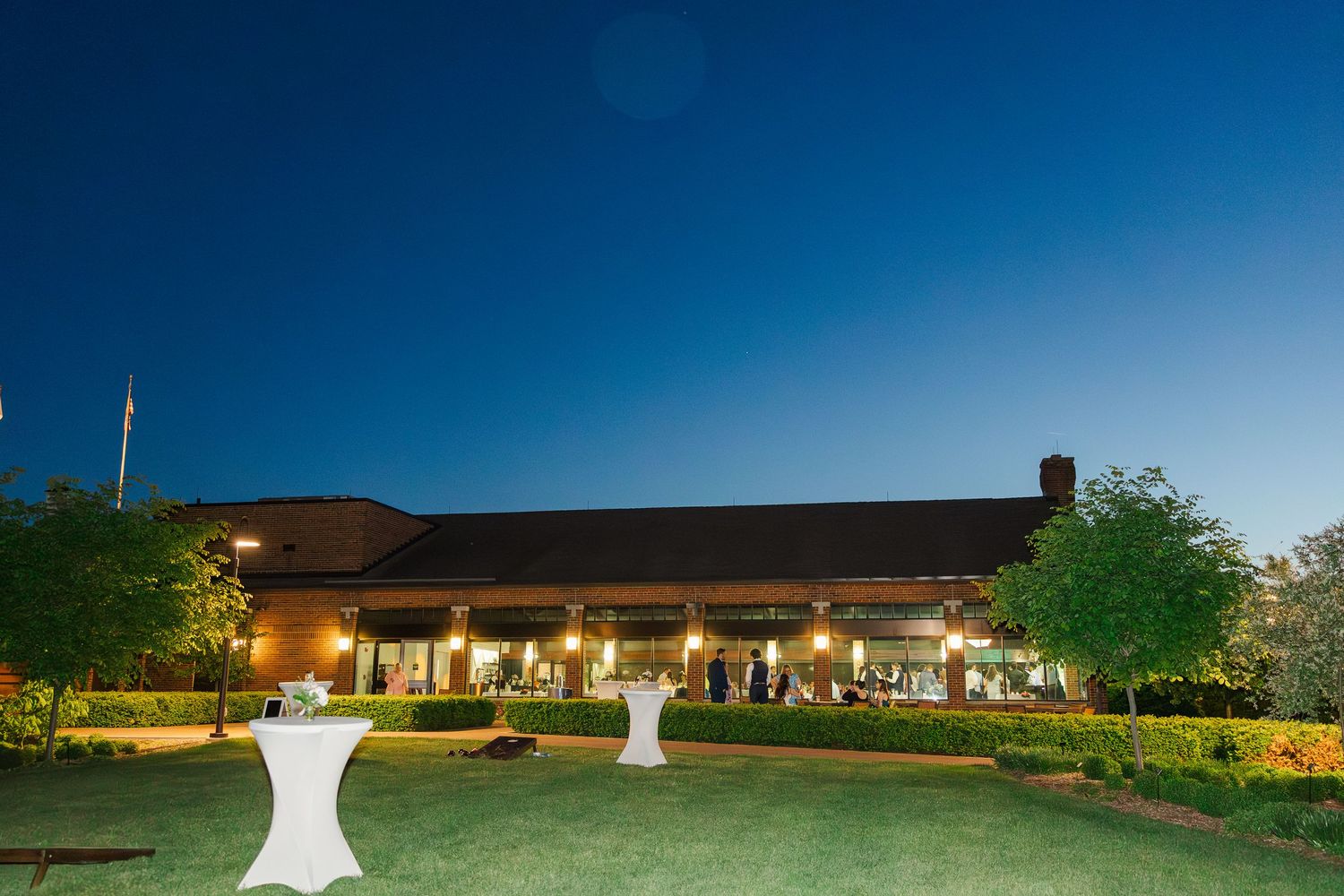 Evening outdoor event setup with illuminated cocktail tables and a beautifully lit venue in the background under clear skies.