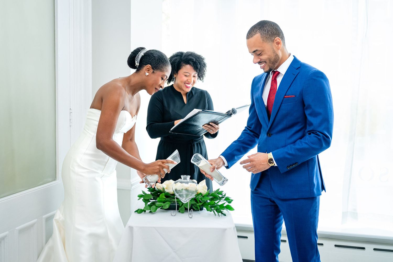 Wedding ceremony taking place in bright white room with officiant and couple at floral decorated altar table.