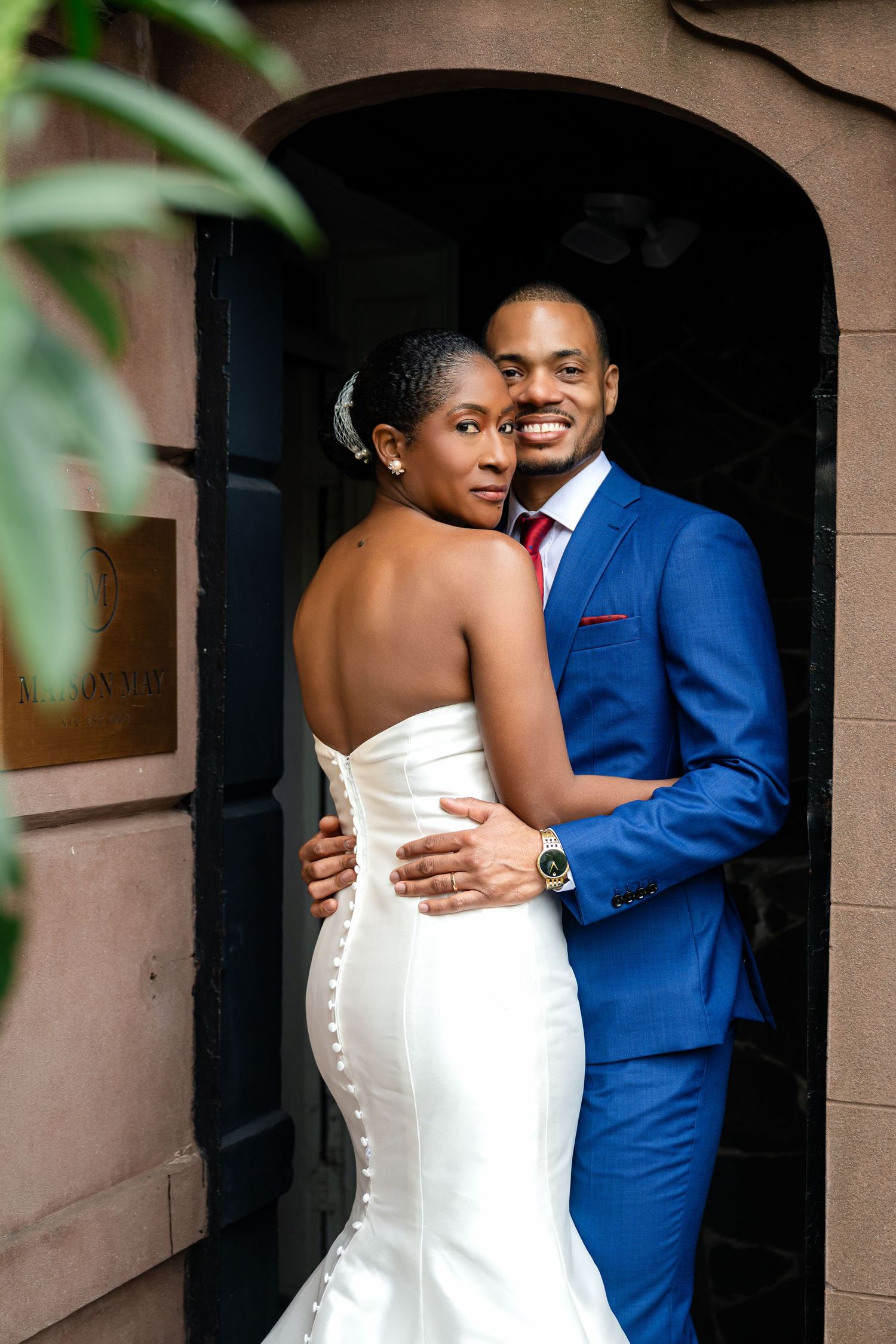 A romantic wedding portrait of a couple in formal attire standing in an elegant doorway.