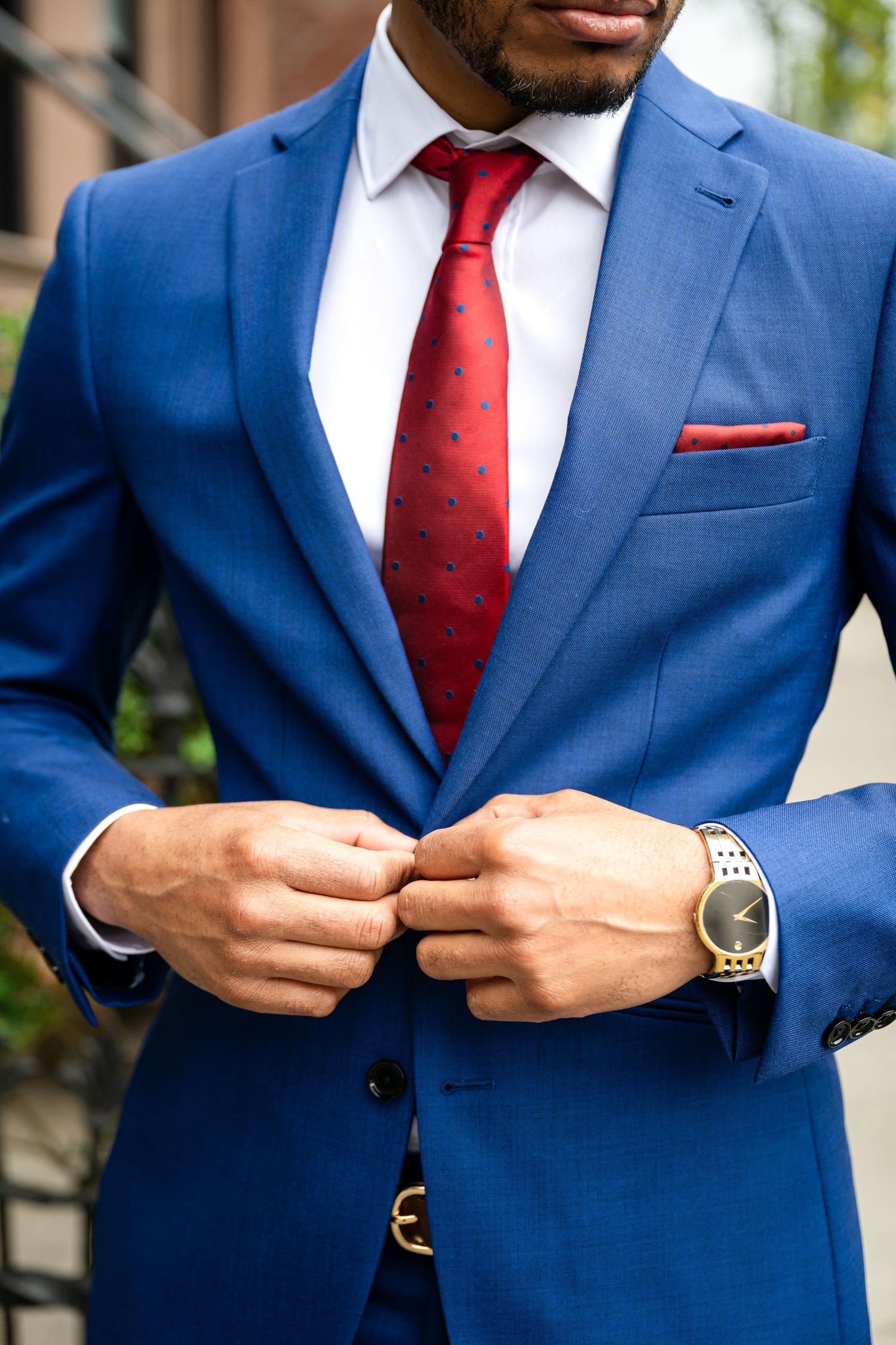 Close-up of royal blue suit jacket with red polka dot tie and silver watch, showing professional business attire details.