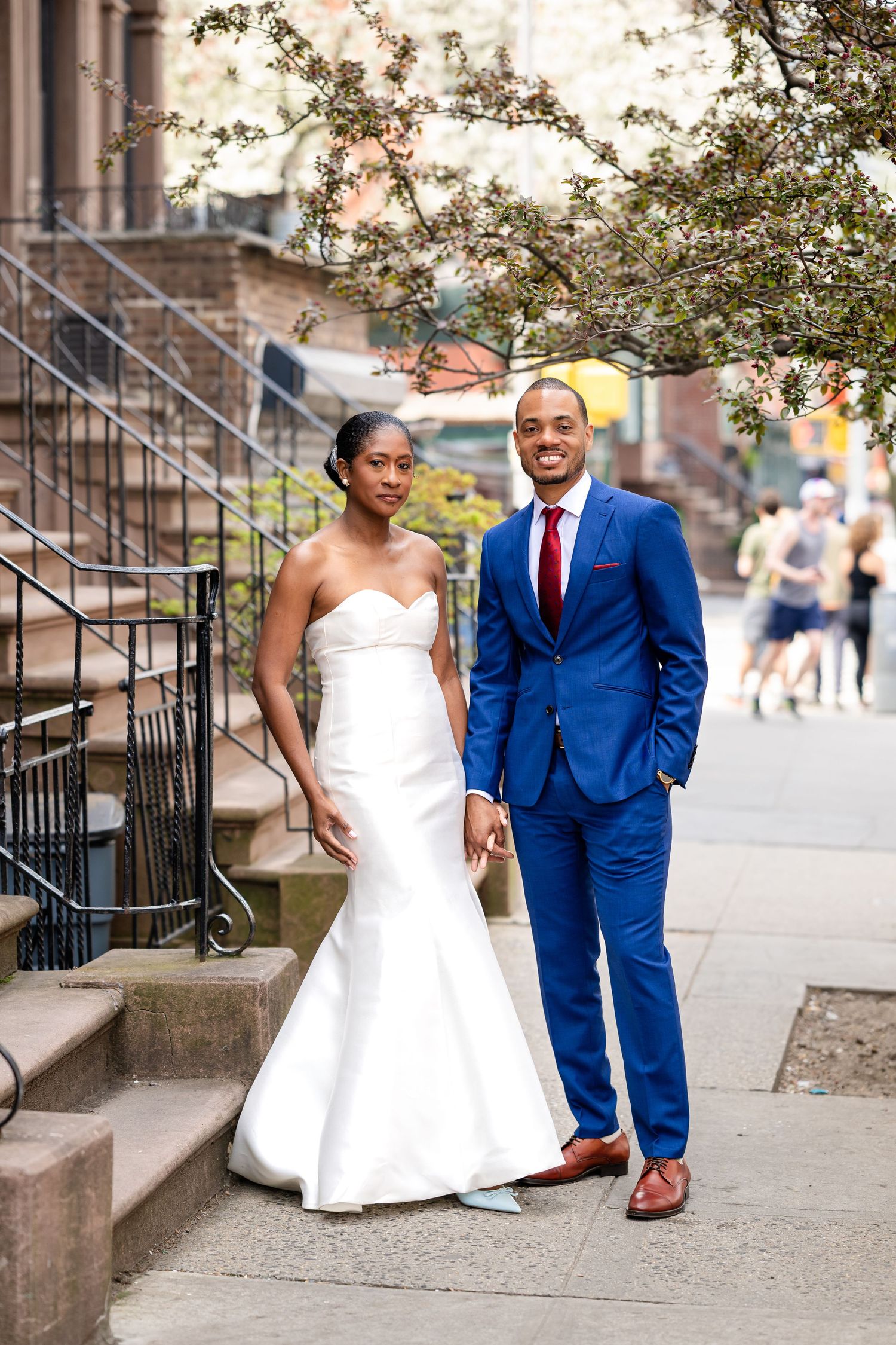 Stylish couple in formal wedding attire poses on urban brownstone steps.