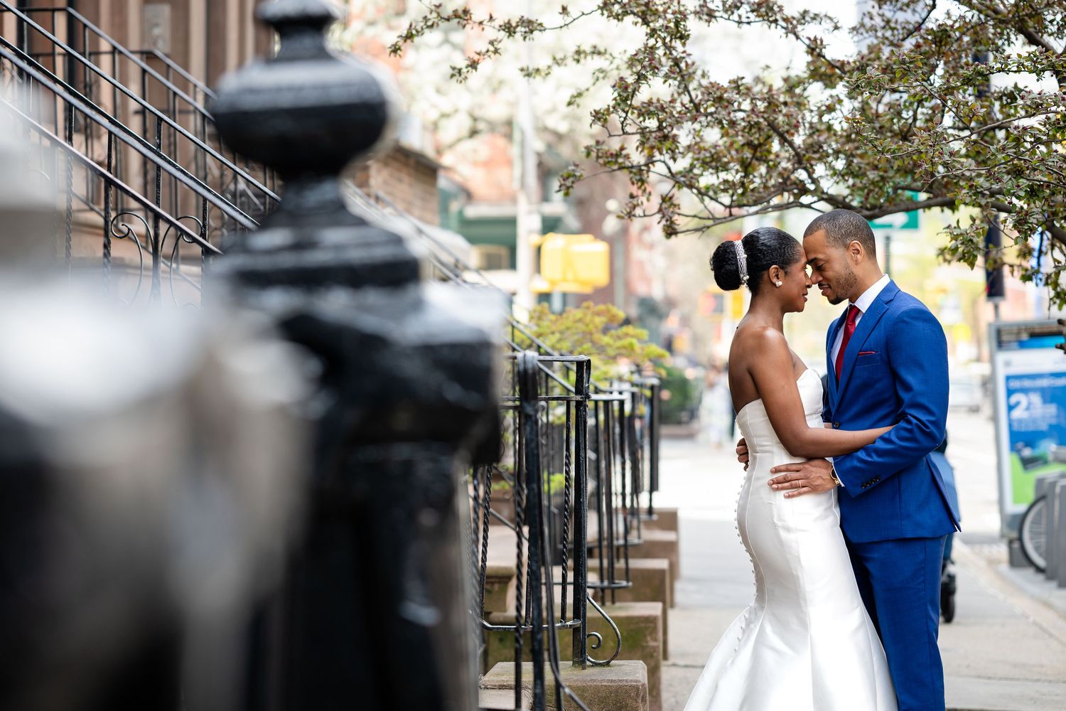 A couple in wedding attire pose for photos on an urban sidewalk.