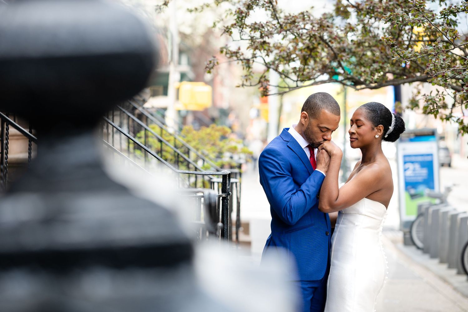 A couple sharing an intimate moment outdoors, with a person in a navy blue suit and white wedding dress.